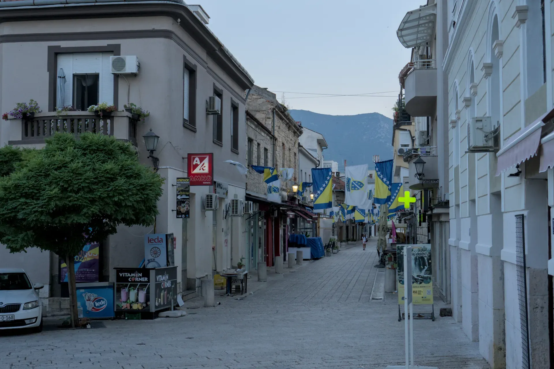Early morning light in Mostar's Old Town, featuring national flags and cobblestone streets.