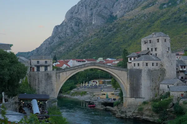 The old Stari Most bridge in Mostar, Bosnia and Herzegovina, captured in the soft light of dawn with a river and mountain backdrop.
