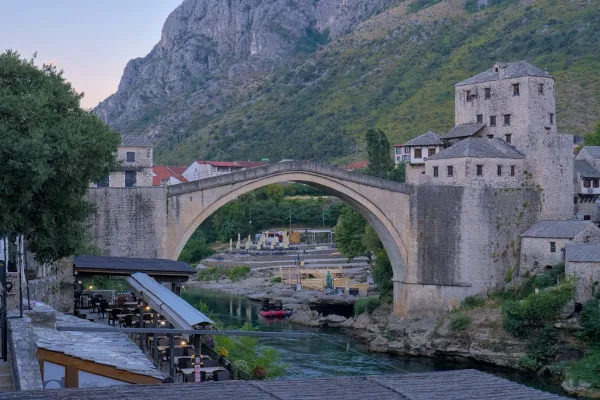 The Old Bridge of Mostar, Bosnia and Herzegovina, set against a mountain backdrop at dawn.