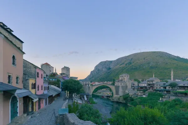 Pre-dawn panorama of Mostar's old town with colorful houses, the historic bridge, and a calm river.