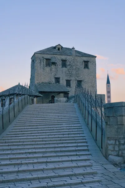 The old Stari Most bridge in Mostar at dawn, featuring stone stairs and historic buildings in the background.