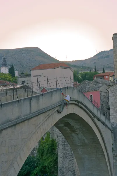 A person is captured mid-jump from Mostar's "Stari Most" (Old Bridge).
