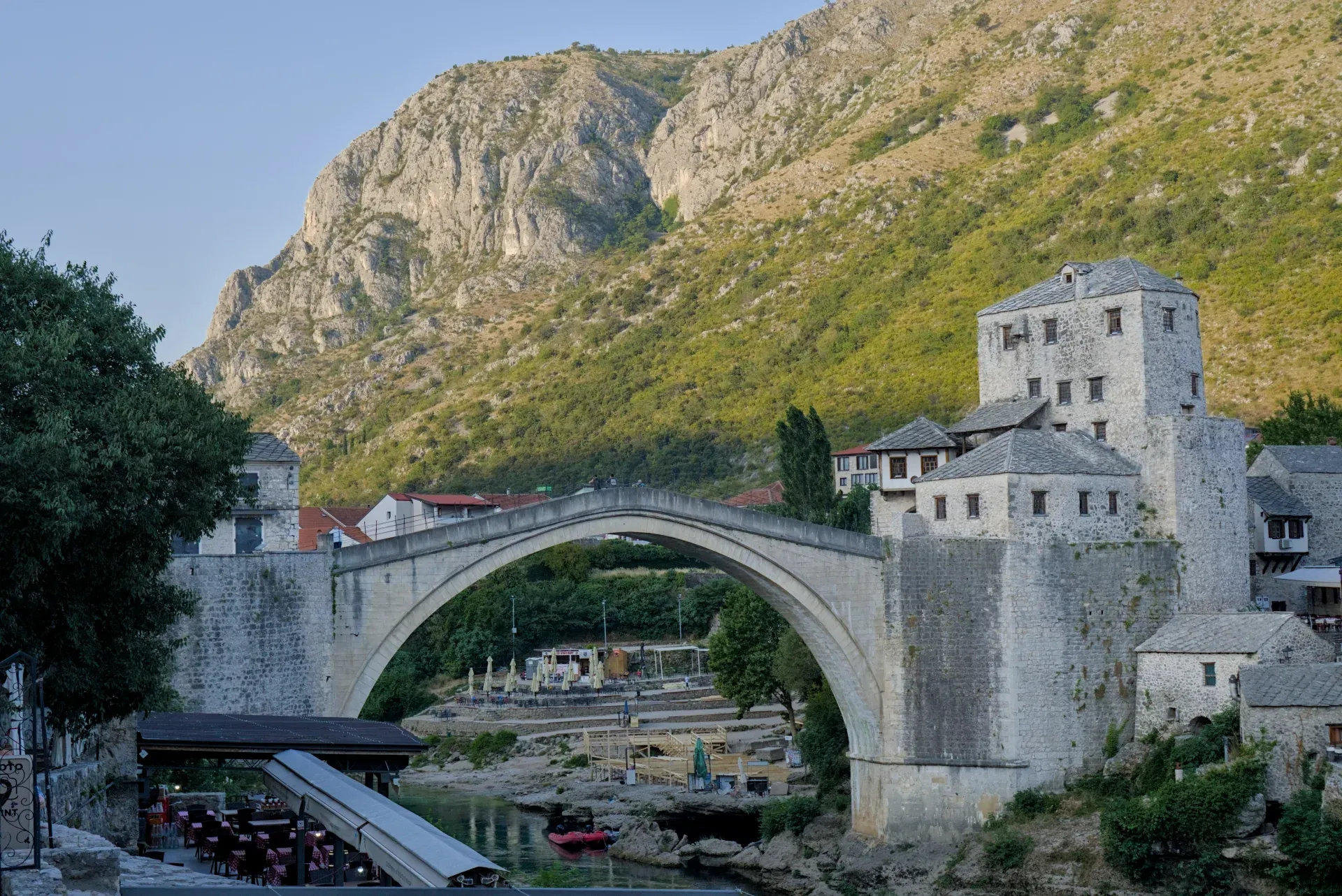 The Old Bridge (Stari Most) in Mostar at sunrise, with a mountain backdrop and river.