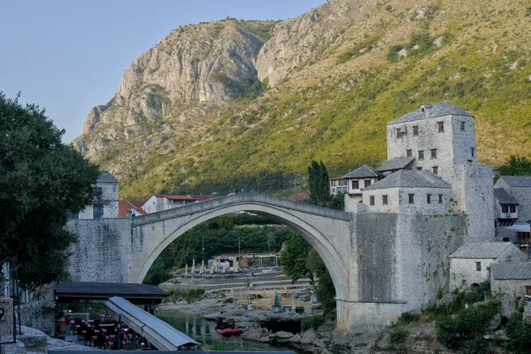 The Old Bridge (Stari Most) in Mostar at sunrise, with a mountain backdrop and river.