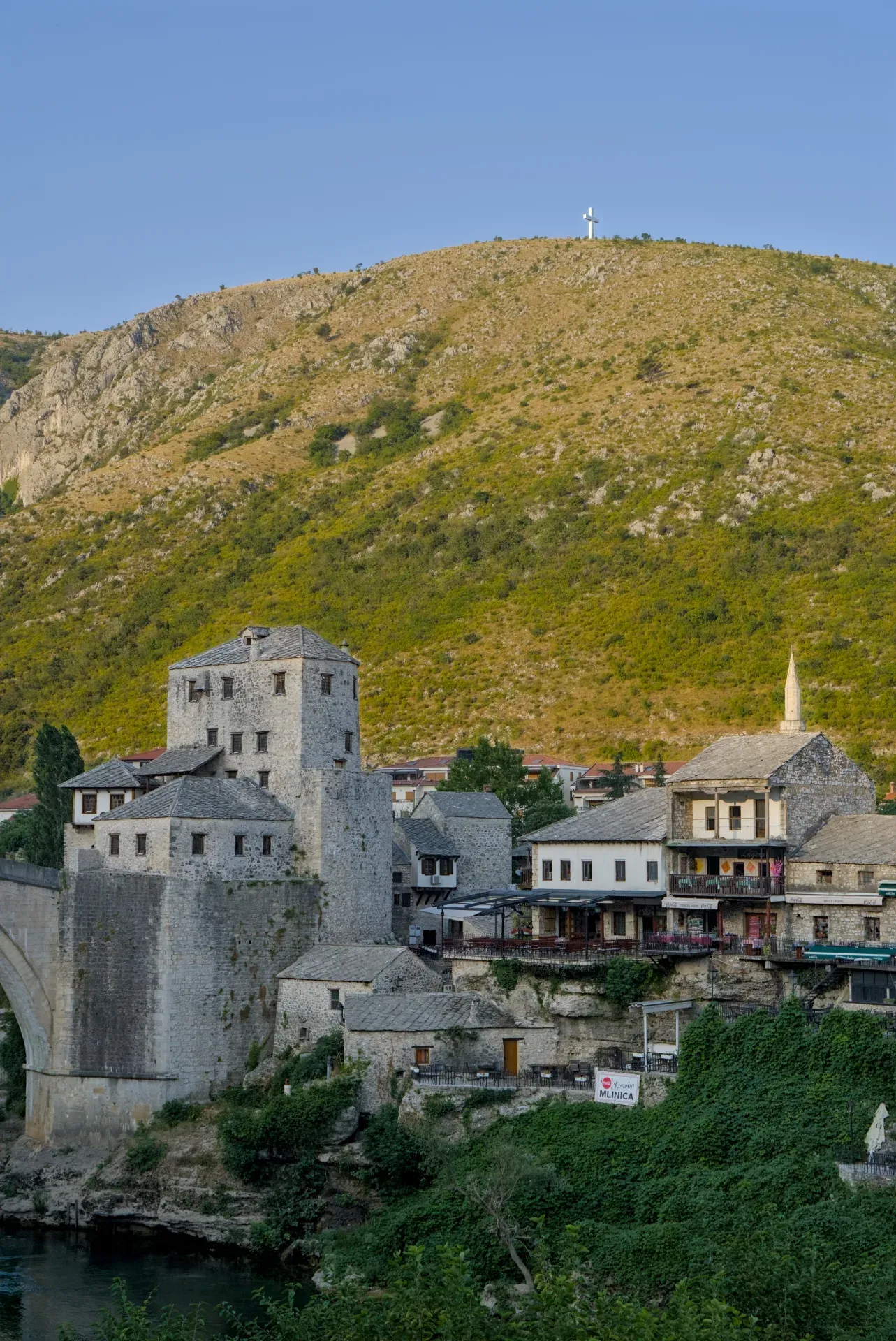 Golden hour over the historic old town of Mostar, featuring stone buildings and a distant mountain.