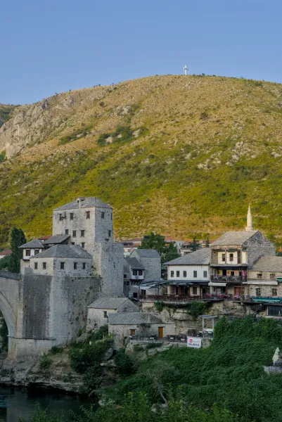 Golden hour over the historic old town of Mostar, featuring stone buildings and a distant mountain.