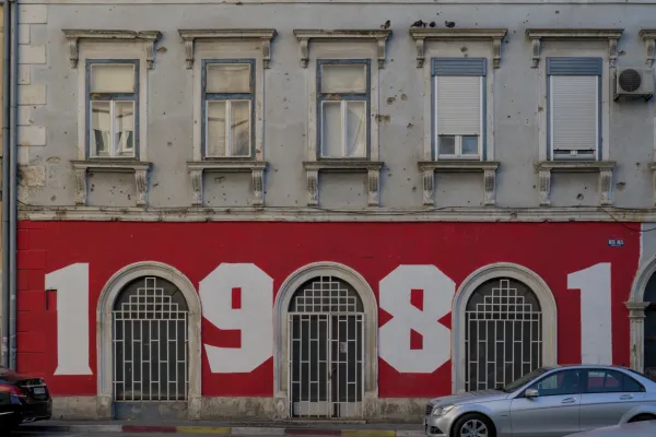 Graffiti "1981" on a red wall in Mostar, Bosnia and Herzegovina, with historical windows and facade details.