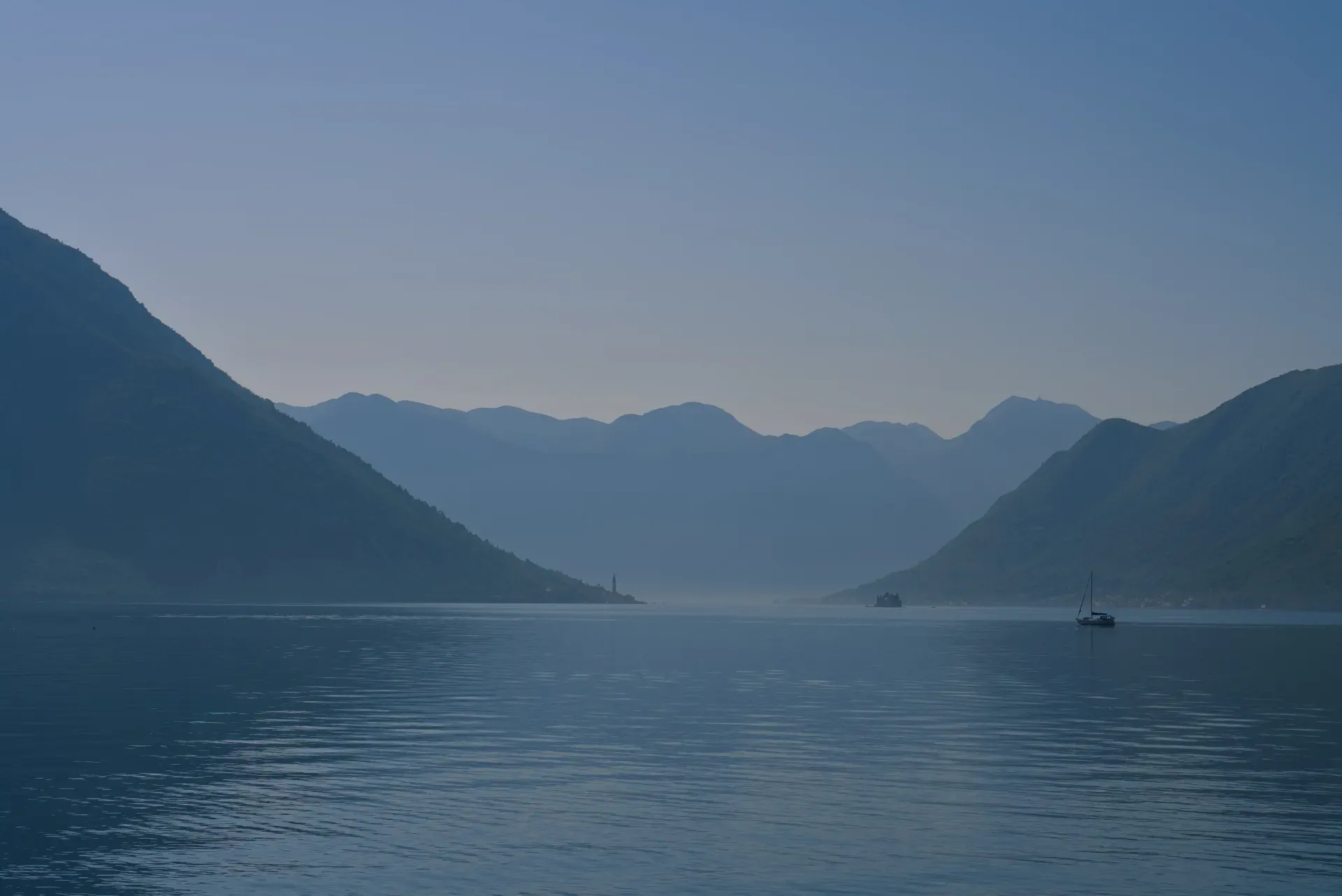 Maglovit jutarnji pogled na Kotorski zaliv, Crna Gora, sa planinama, vodom, jedrenjakom i dalekim pogledom na Perast.