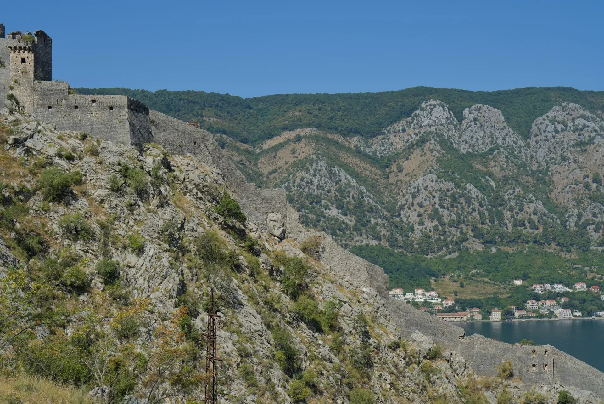 Pogled sa planine na istorijske zidine Kotorske tvrđave, Crna Gora, sa zelenim brdima u pozadini.