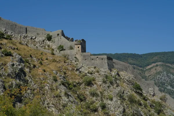 The старинные крепостные стены на скале of Kotor, Montenegro, stand majestically against a clear blue sky.