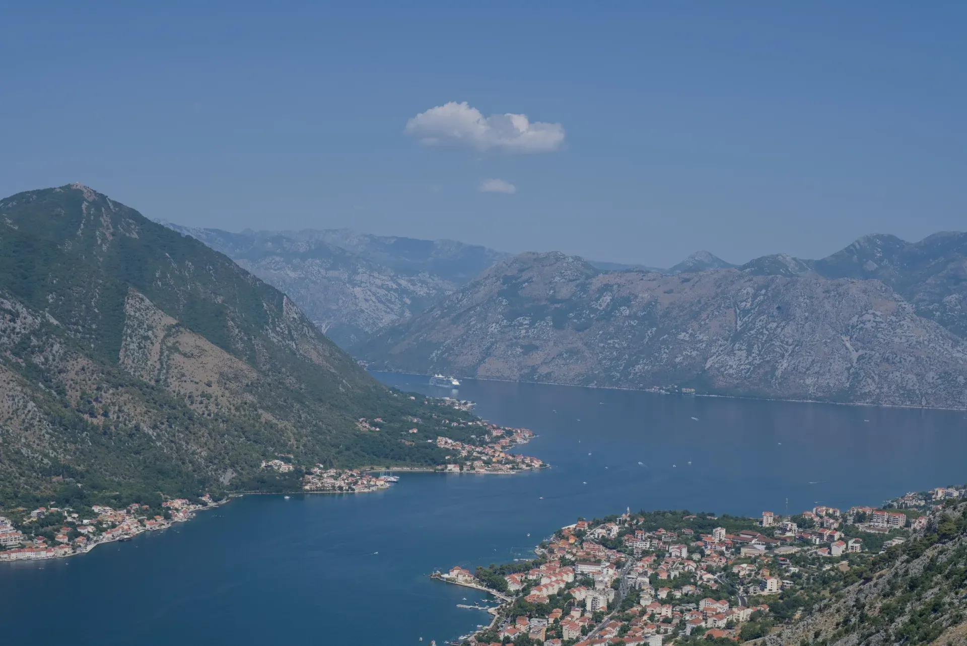 Aerial view of a cruise ship entering Kotor Bay, overlooking the coastal towns of Dobrota and Prcanj.