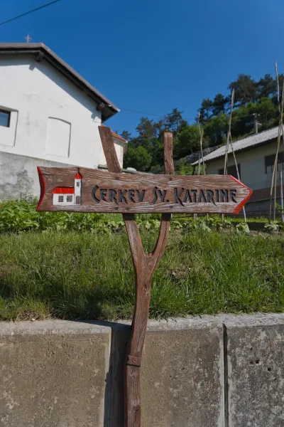 A wooden signpost reading 'CERKEV SV. KATARINE' indicates the direction to the church, on the way to Predjama.