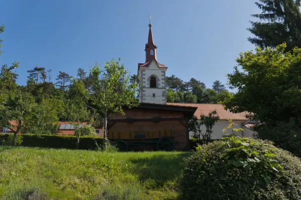 A picturesque village church with a red spire and wooden shed with an old cart, on the route to Predjama Castle, Slovenia.