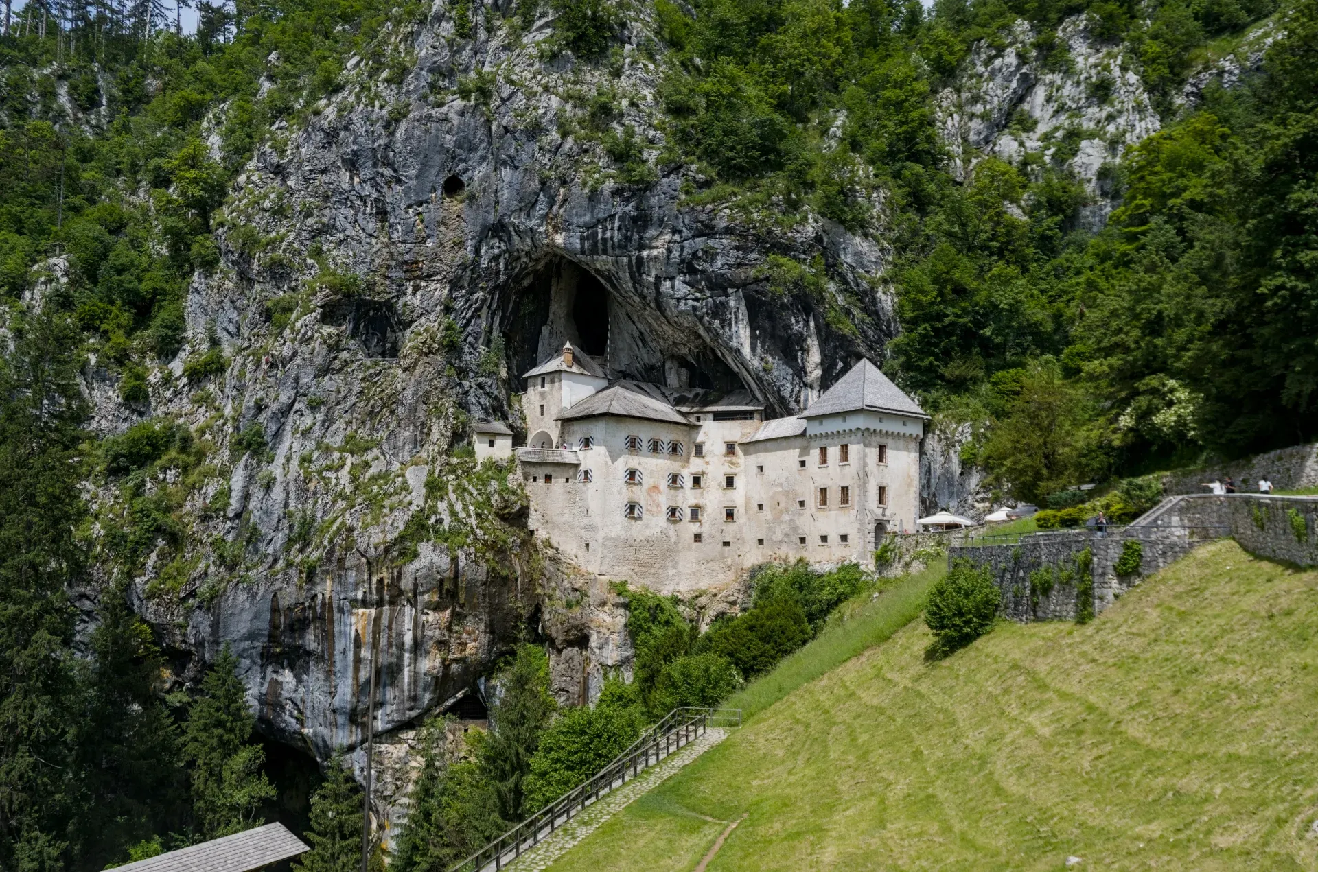 The historic Predjama Castle stands majestically from a vertical cliff face in Slovenia, surrounded by lush greenery.