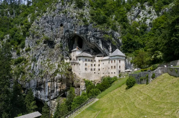 The historic Predjama Castle stands majestically from a vertical cliff face in Slovenia, surrounded by lush greenery.