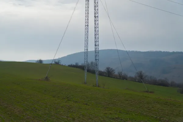 A tall power pole stands prominently on the rolling green hills of Fruska, Serbia, under an overcast sky.