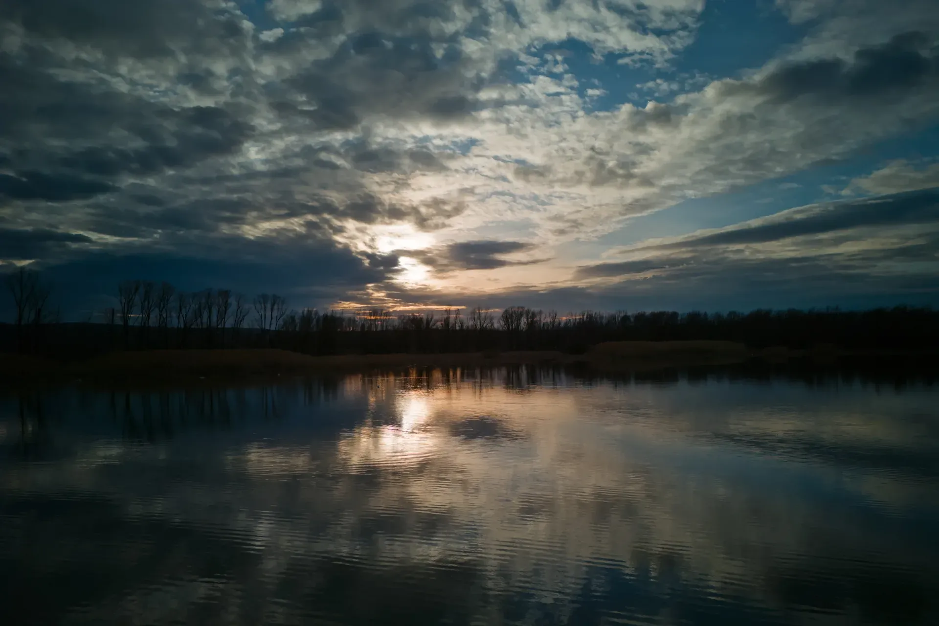 Drammatico tramonto sull'acqua a Begečka Jama vicino a Novi Sad, con nuvole e riflessi.