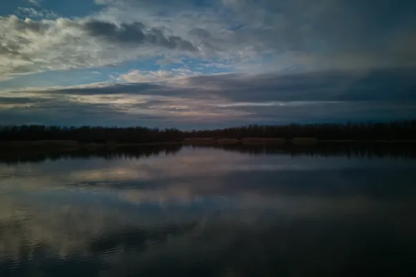 Begečka Jama before sunset, featuring dramatic clouds reflected on calm water surface.