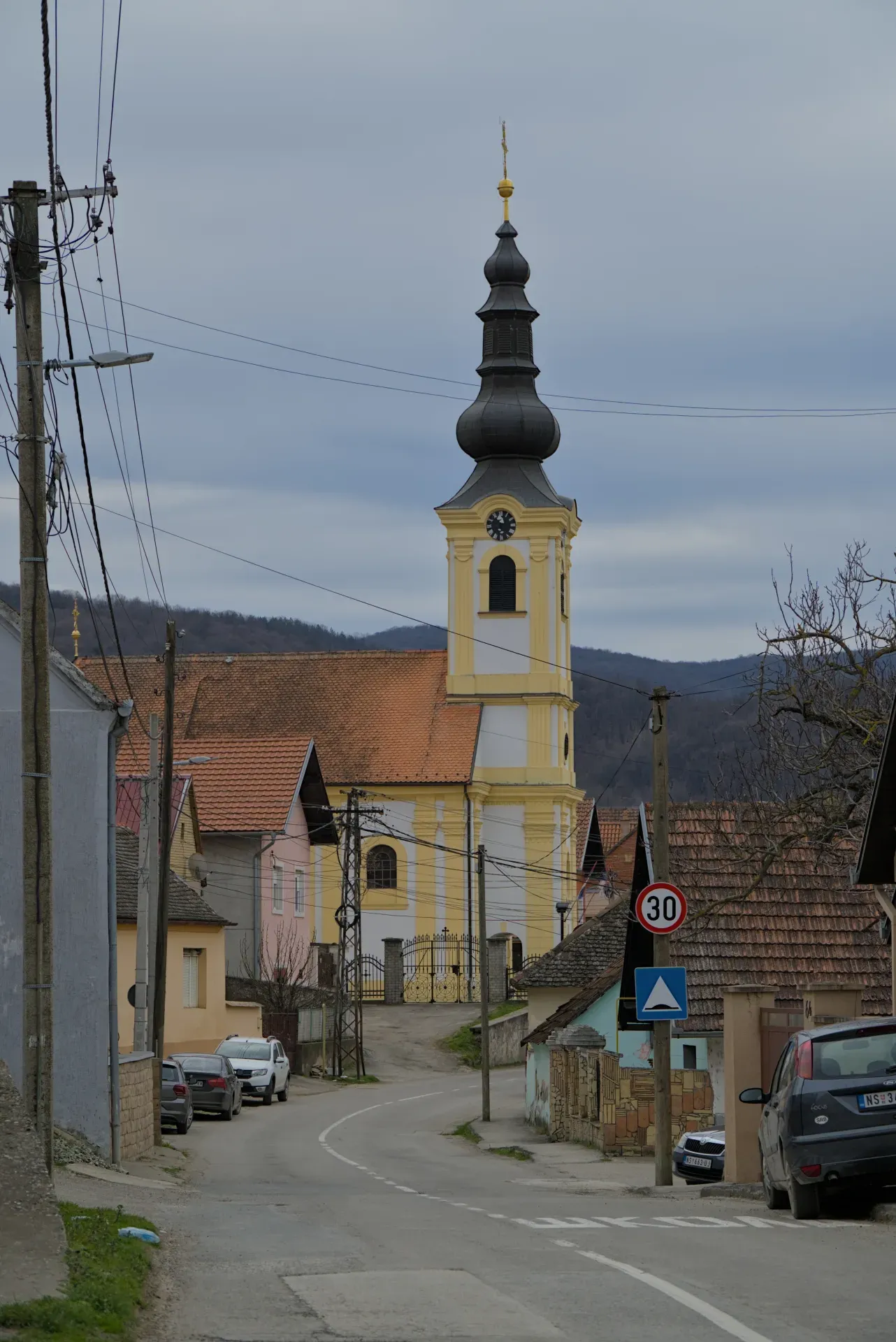 The Church of the Transfiguration in Beočin, Serbia, with its distinctive yellow and white bell tower, under an overcast sky.