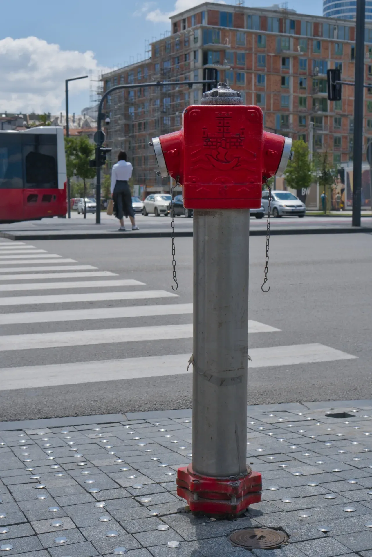 A red hydrant stands on a paved street in Belgrade, next to a crosswalk and an unfinished building.