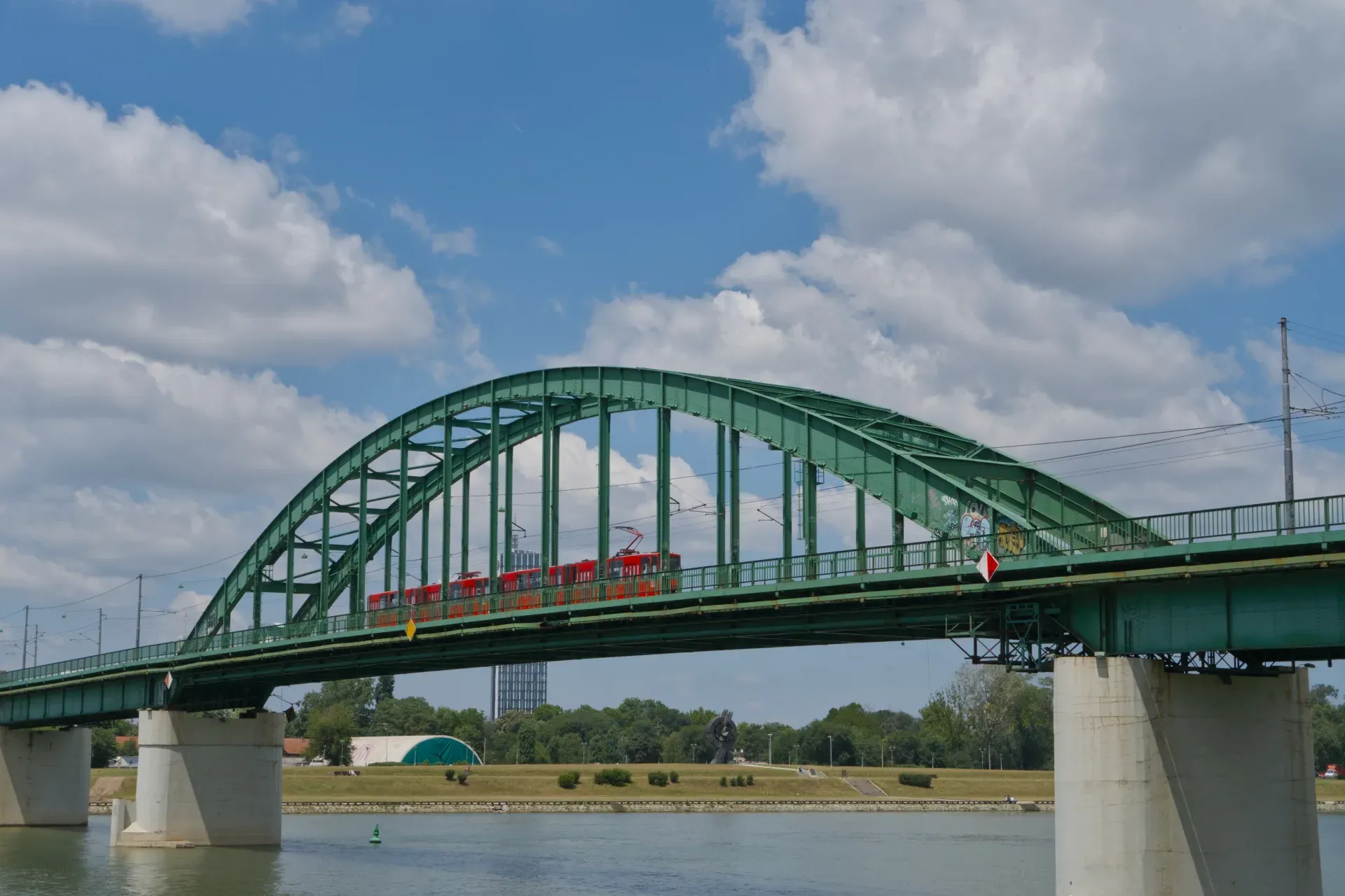 The Old Sava Bridge in Belgrade with a red tram passing over it against a blue sky.