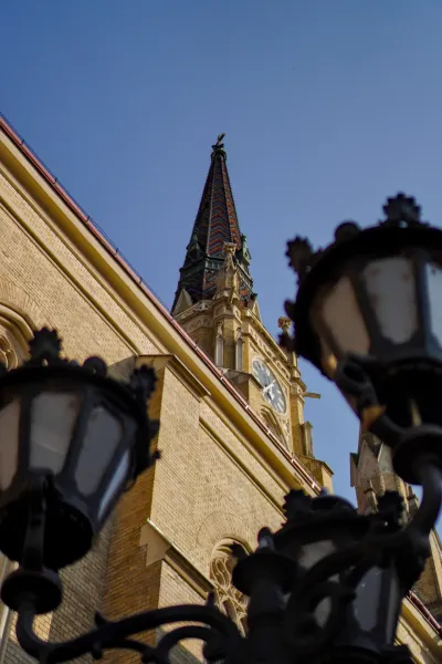 Photo of the Church of the Virgin Mary in Novi Sad, Serbia, featuring a tiled roof and clock, captured from a low angle.