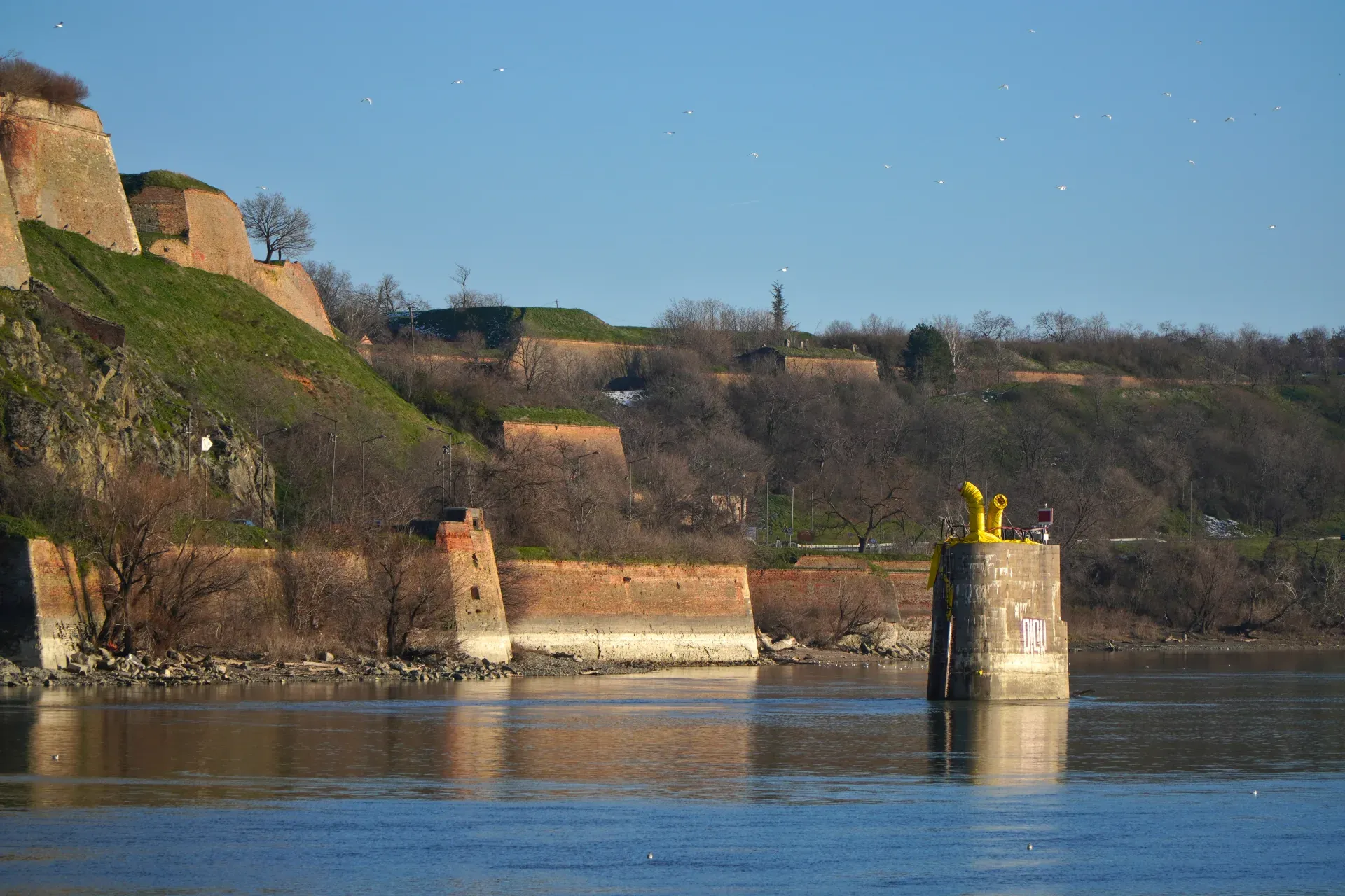 Muri di pietra della Fortezza di Petrovaradin si ergono sopra le acque blu del Danubio sotto un cielo limpido, creando un paesaggio storico.