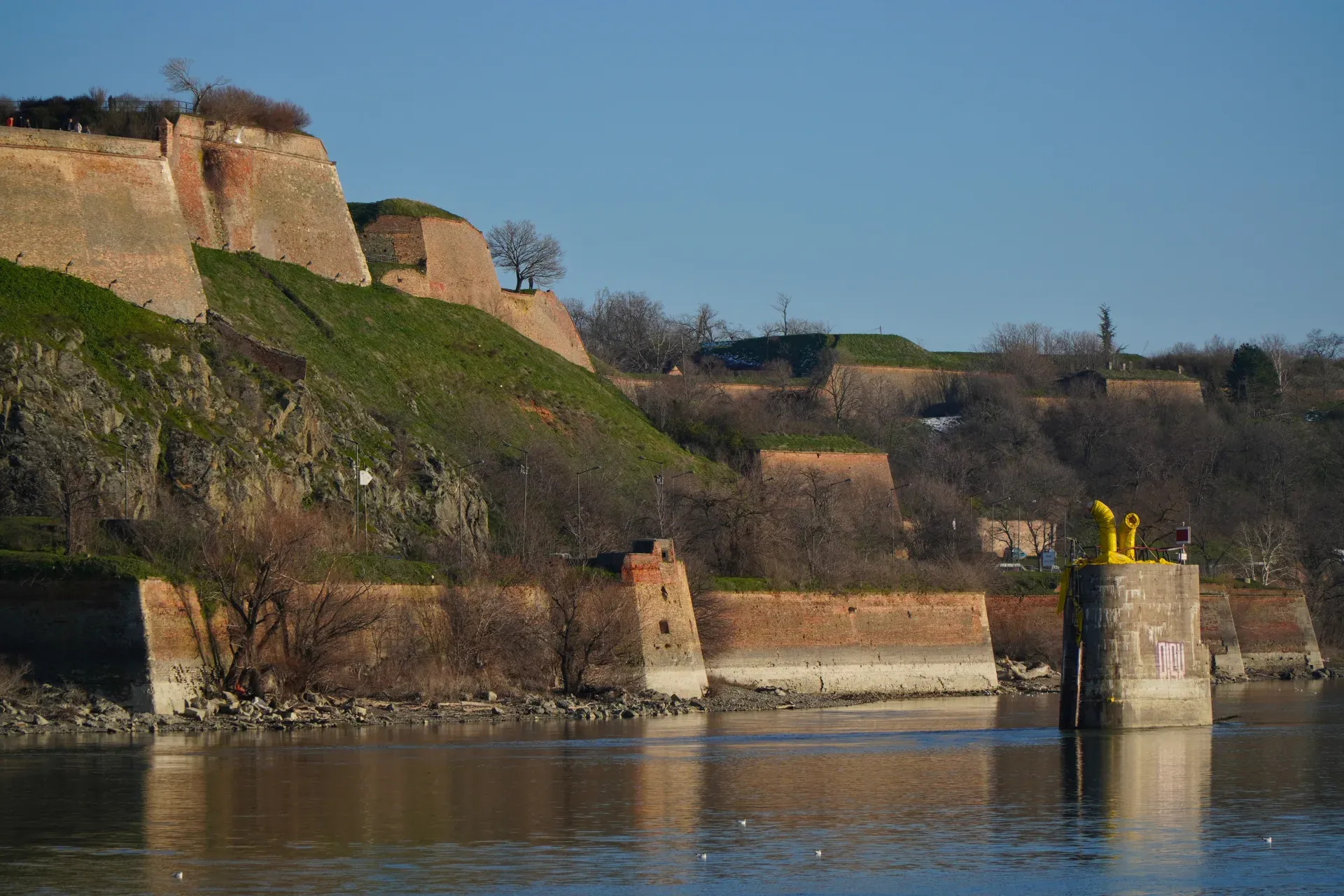 Vista del Danubio e delle antiche mura di mattoni della Fortezza di Petrovaradin sotto un cielo limpido.