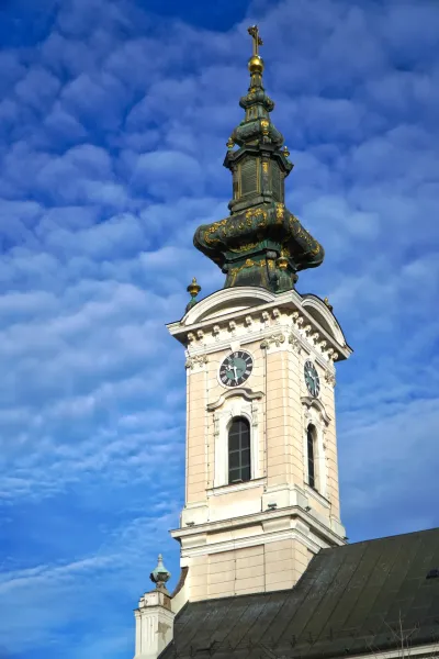 Tower of Saint George Church in Novi Sad with a clock against a blue sky with clouds.