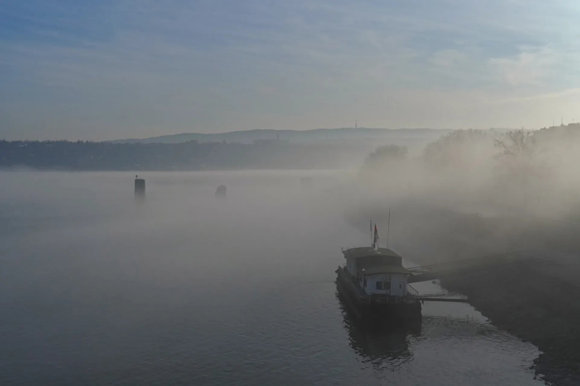 Jetée sur le Danube dans un brouillard dense avec un bateau près du rivage, créant une atmosphère mystérieuse.