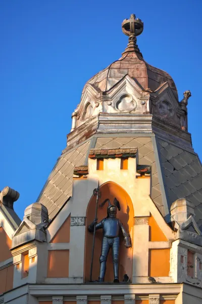 Knight statue on the roof of the Queen Palace Hotel in Novi Sad, Serbia, with a blue sky in the background.