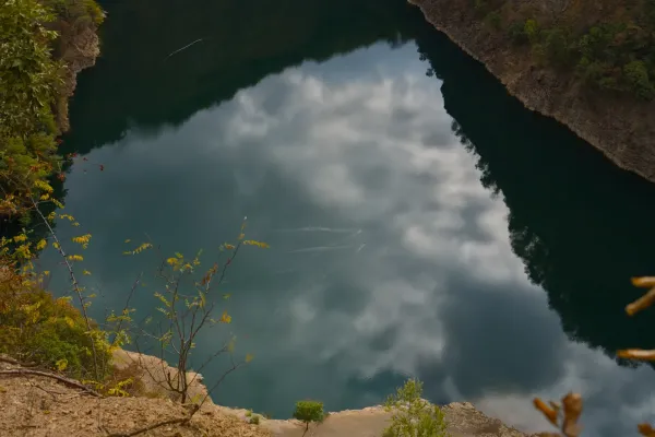 Two ducks swim leisurely across the mirror-like surface of Ledinačko Lake, reflecting the clouds. View from the rock.