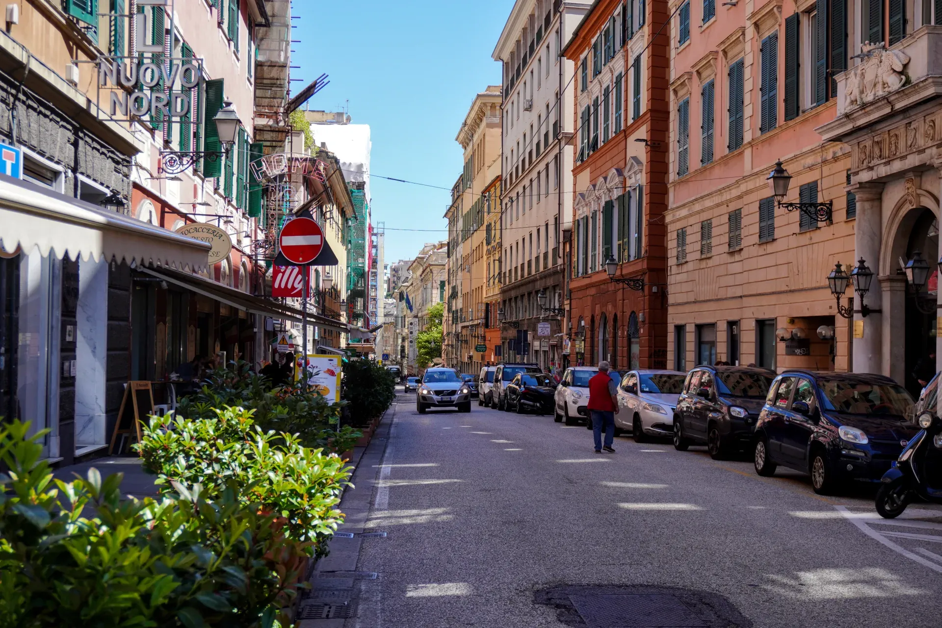 Street view of Via Balbi in Genoa Italy with historic buildings and parked cars under a blue sky.