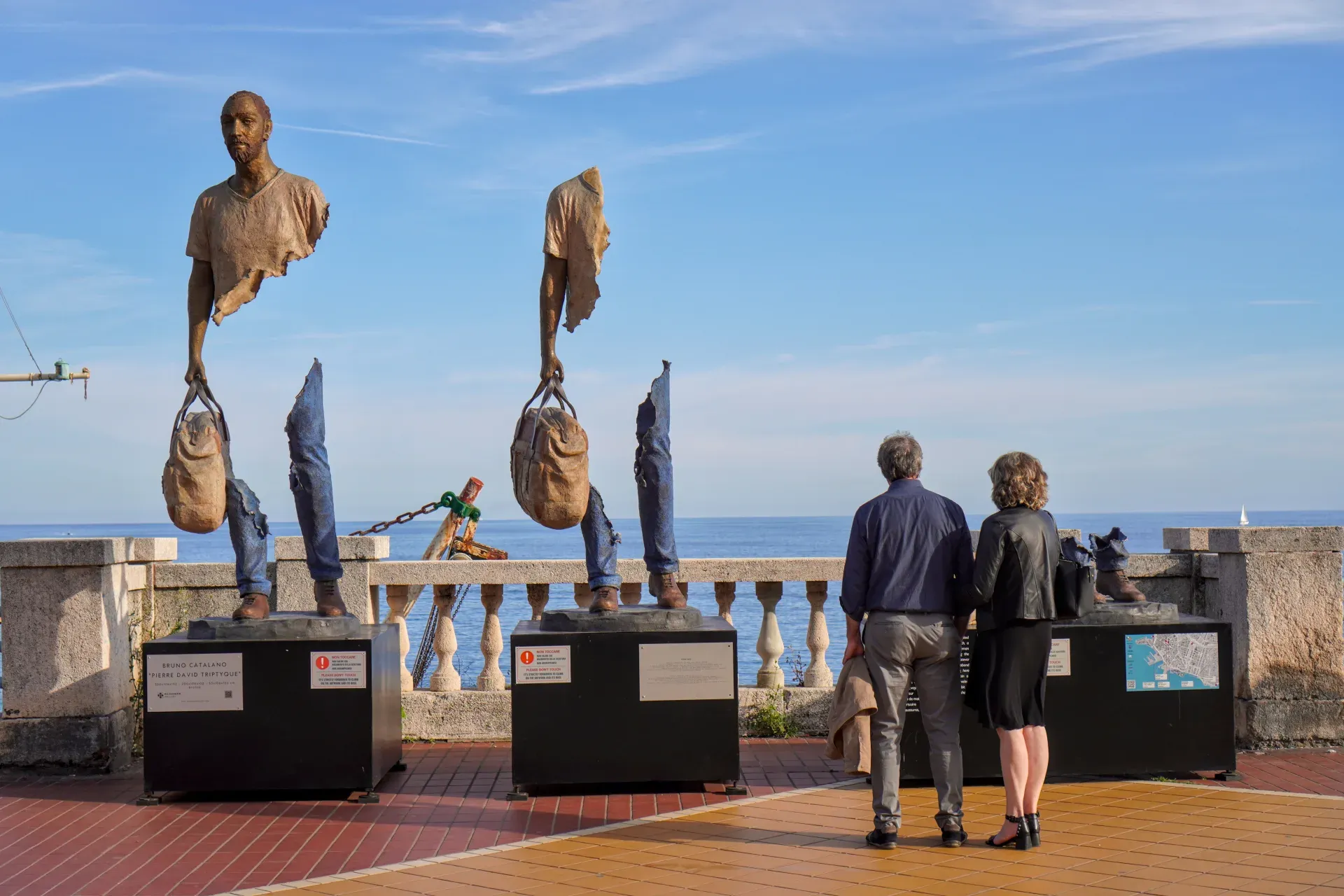 Una collezione di torri di pietra ed edifici residenziali si trova su una collina densamente boscosa a Genova, Italia, sotto un cielo blu brillante.