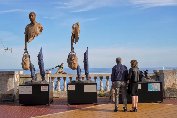 Una collezione di torri di pietra ed edifici residenziali si trova su una collina densamente boscosa a Genova, Italia, sotto un cielo blu brillante.