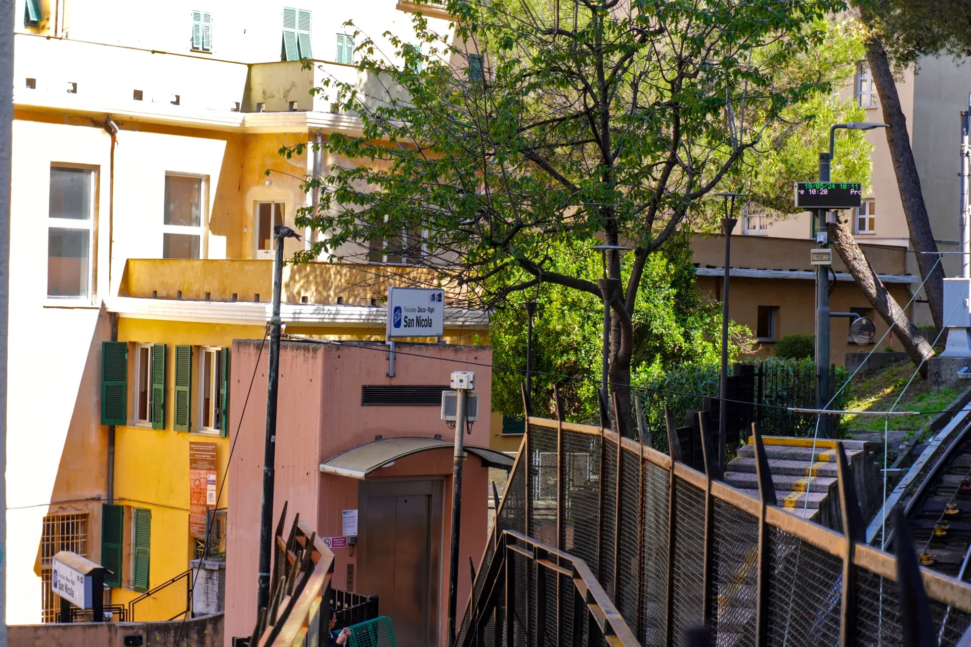 Pogled na zgradu stanice Funicolare San Nicola u Đenovi, Italija, sa fasadom boje breskve, modernim liftom i signalizacijom za Funicolare Zecca – Righi.