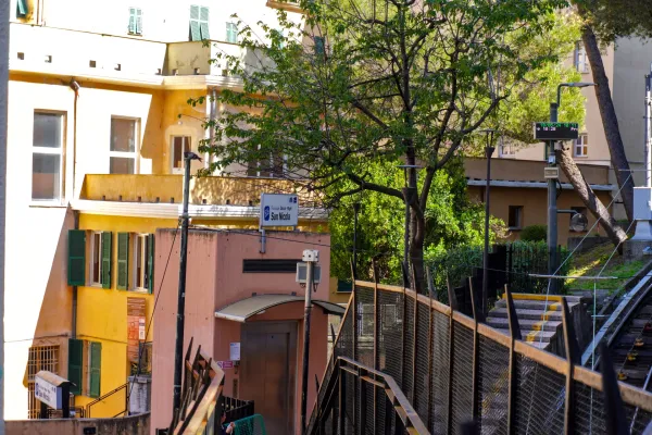 Ein Blick auf das Stationsgebäude der Funicolare San Nicola in Genua, Italien, mit einer pfirsichfarbenen Fassade, einem modernen Aufzug und einem Schild für die Funicolare Zecca – Righi.