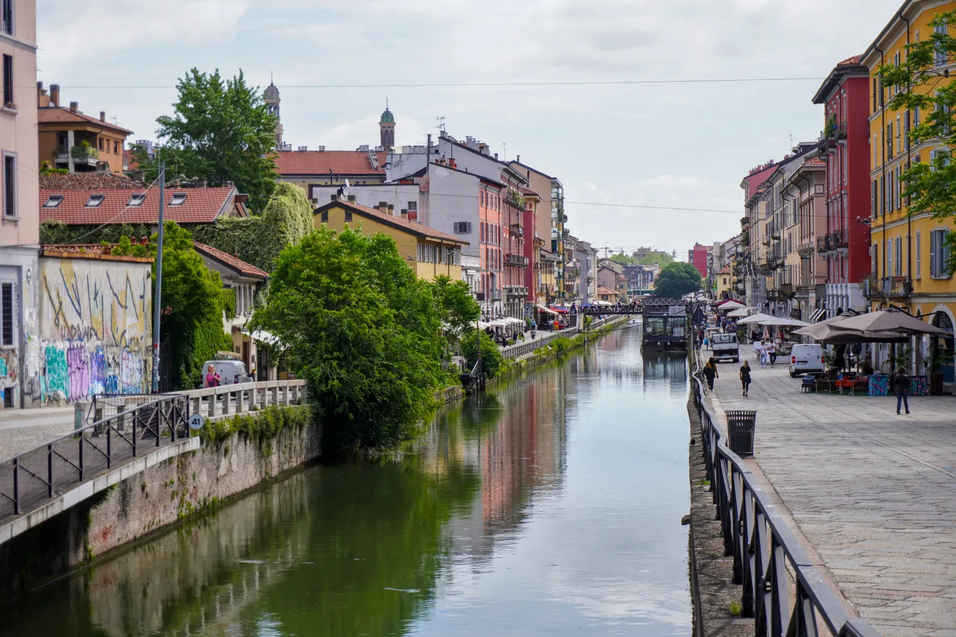 Kanal u milanskom kvartu Navigli sa šarenim zgradama, plutajućom strukturom nazvanom 'Square Garden', čamcem i skuterom.