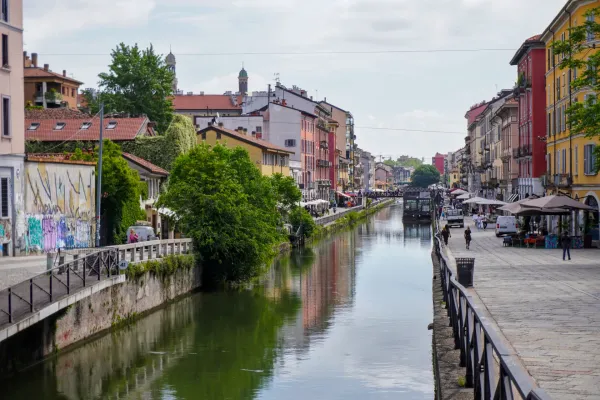 Ein Kanal im Mailänder Navigli-Viertel mit bunten Gebäuden, einer schwimmenden Struktur namens 'Square Garden', einem Boot und einem Roller.