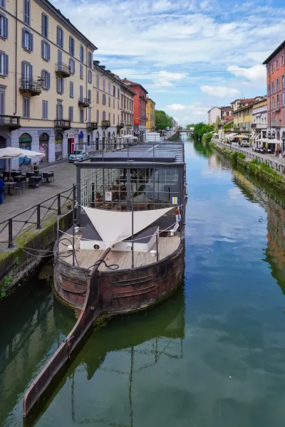 Una vista dei canali Navigli a Milano, Italia, con edifici residenziali colorati che costeggiano il corso d'acqua e biciclette parcheggiate lungo il marciapiede in pietra.