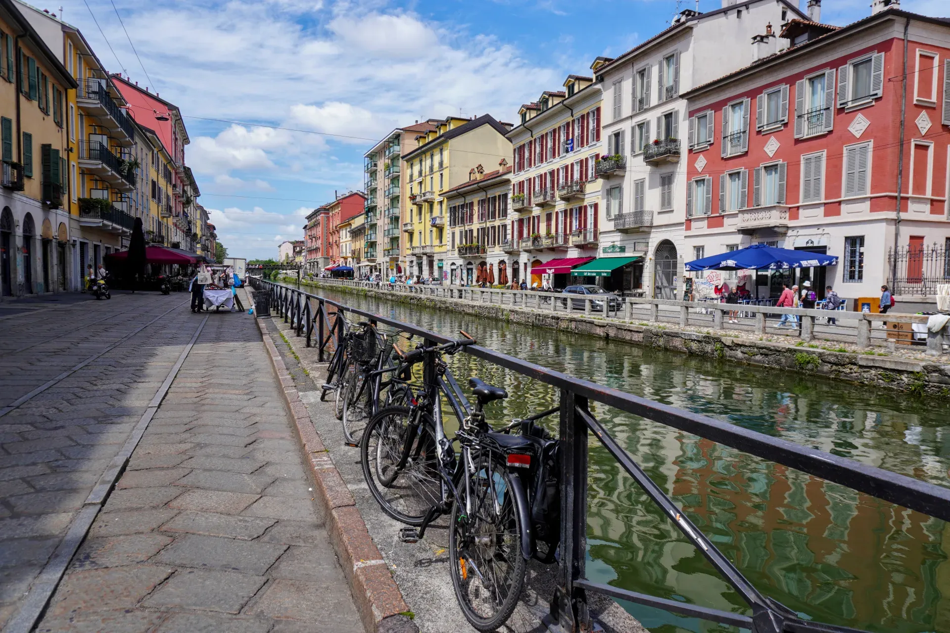 Un canal dans le quartier Navigli de Milan avec des bateaux dragons en course, bordé d'immeubles colorés et de sièges extérieurs.
