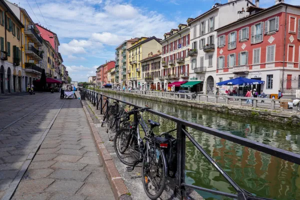 Un canale nel quartiere Navigli di Milano con dragon boat in gara, fiancheggiato da edifici colorati e posti a sedere all'aperto.