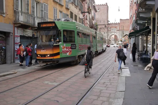 Eine gelbe Straßenbahn auf einer Kopfsteinpflasterstraße in Mailand mit Gebäuden und Cafés an den Seiten.