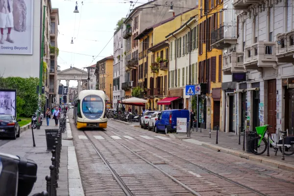 Un tram giallo e bianco percorre una strada di Milano con edifici d'epoca e negozi ai lati.