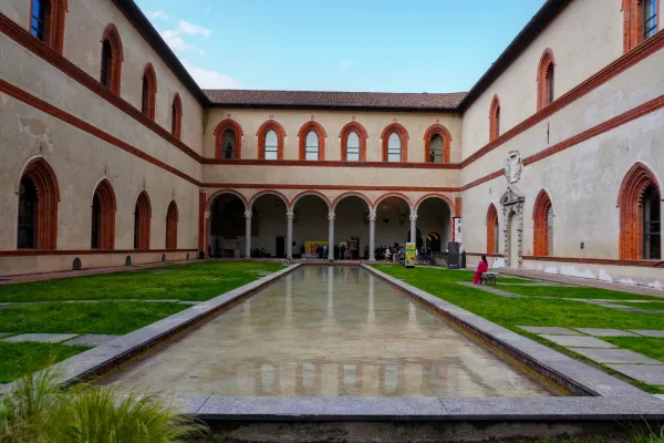 Innenhofansicht des Castello Sforzesco in Mailand, Italien, mit arkadengeschmückten Gebäuden, gepflegten Rasenflächen und einem reflektierenden Wasserbecken.