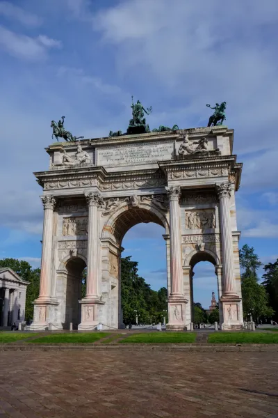 Der Arco della Pace, ein großer neoklassizistischer Bogen, gekrönt von einer Quadriga-Skulptur unter einem strahlend blauen Himmel mit vereinzelten Wolken.