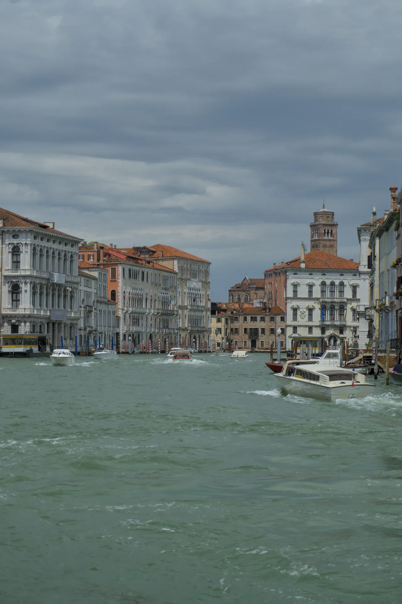 Barche sul Canal Grande a Venezia, Italia, con edifici decorati e un campanile sullo sfondo sotto un cielo nuvoloso.